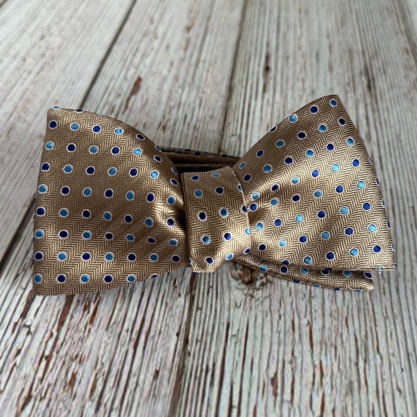 American made mocha colored bowtie with blue dots sitting on a wood table