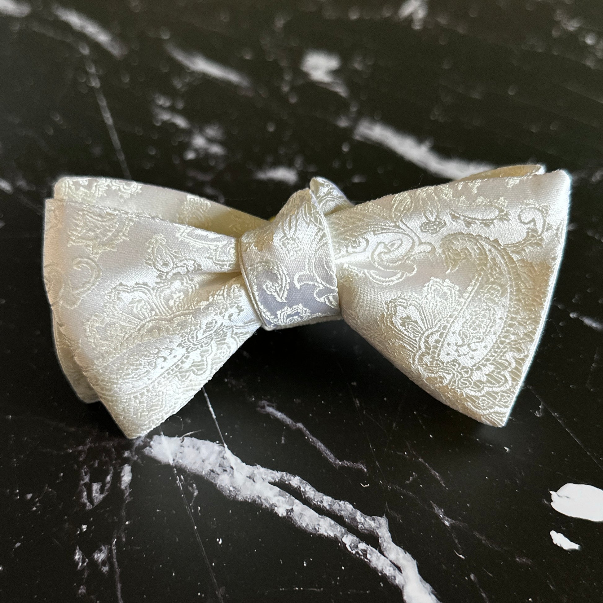 White silk bowtie with paisley pattern on black marble tabletop