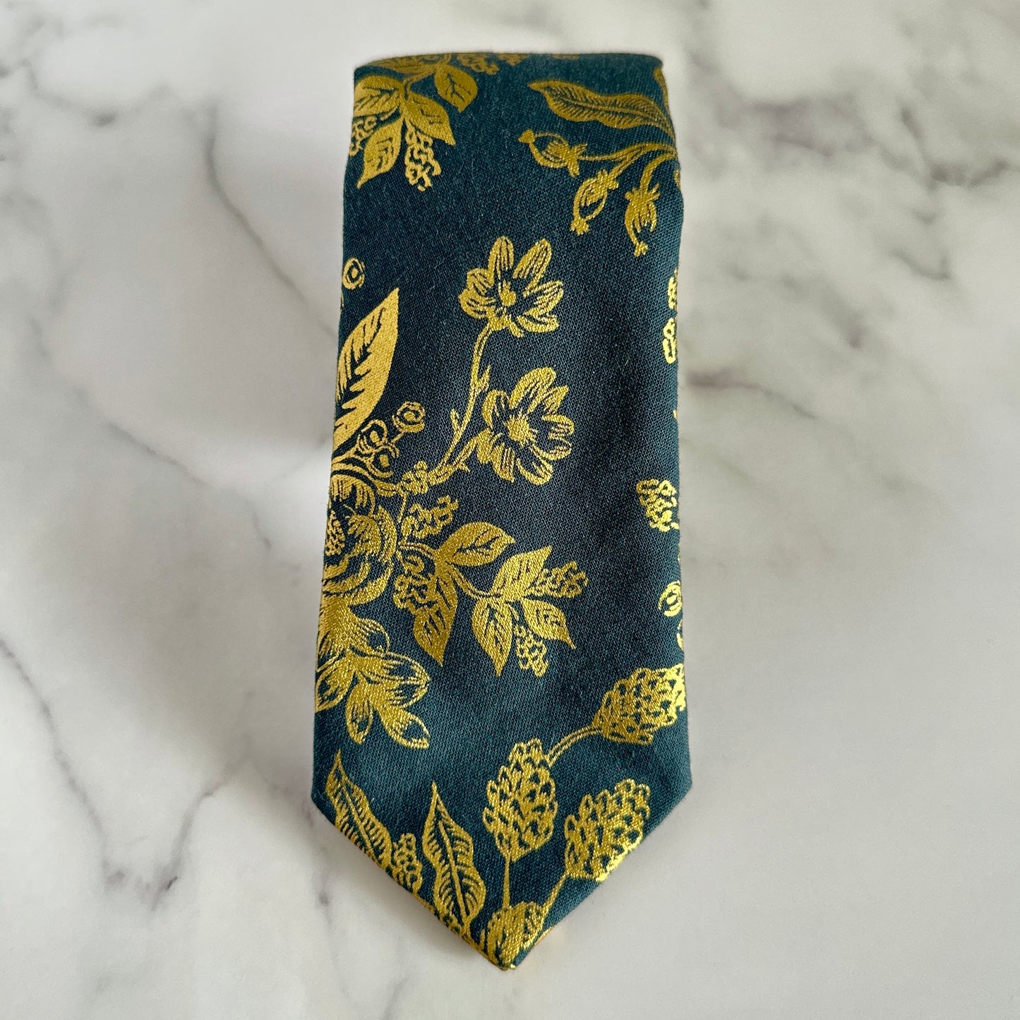 American made blue neck tie with gold floral pattern on marble tabletop