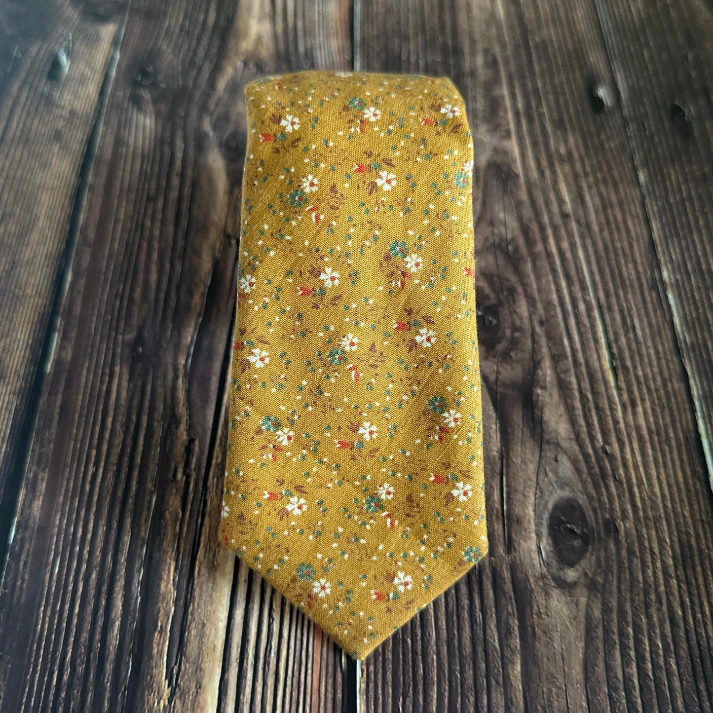 American made golden necktie with floral pattern sitting on a wood table