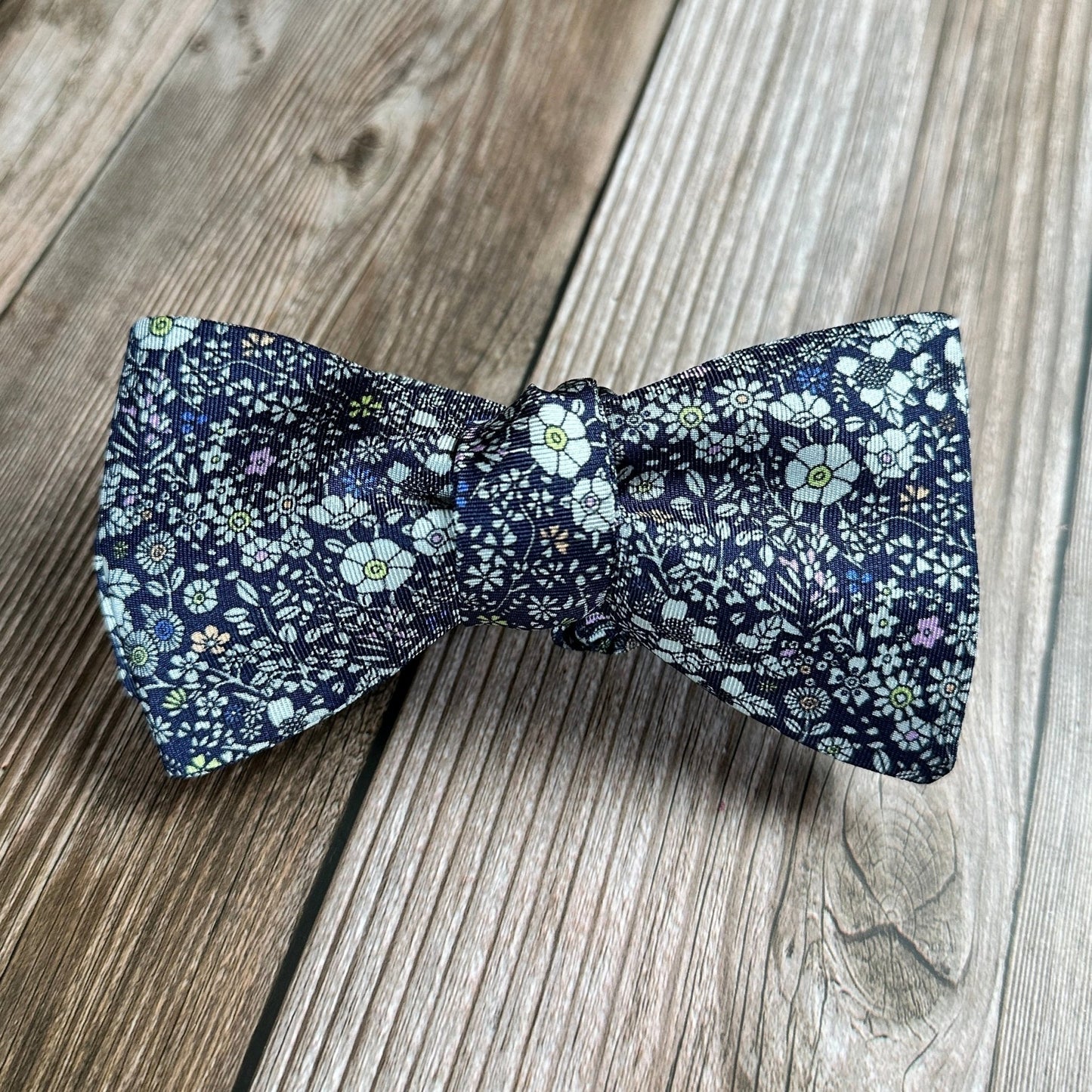 American made blue bowtie with multicolored flowers on wood table